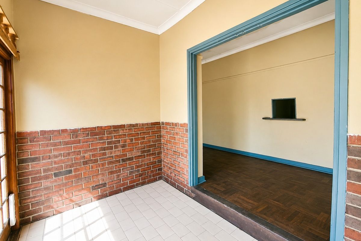 An empty living area featuring a combination of parquet and ceramic tile flooring, brick wainscoting, and a built-in wall shelf.