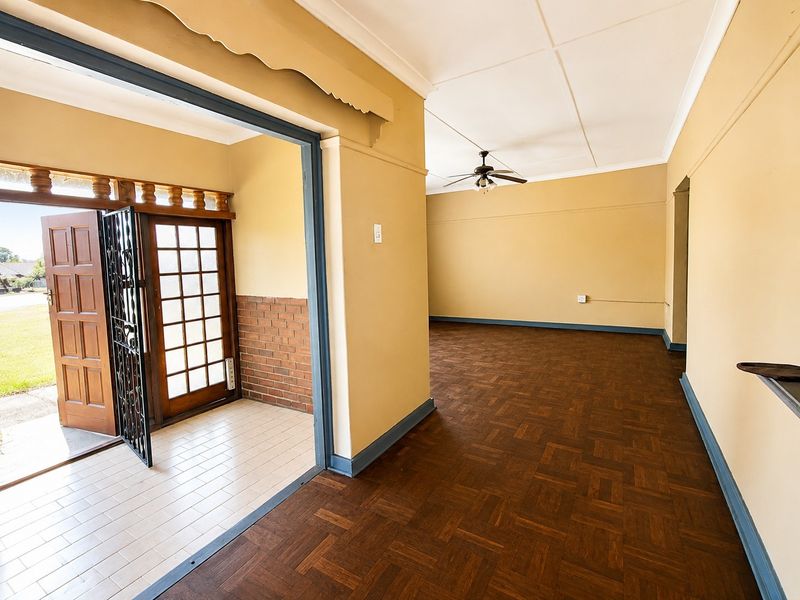 Spacious living area featuring classic parquet flooring, a ceiling fan, and a tiled entryway with a secure timber door and brick accents.