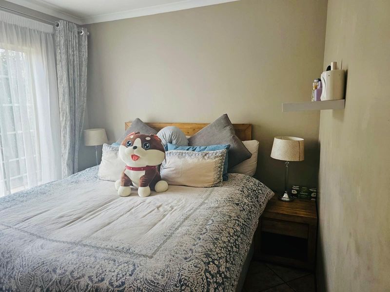 A cozy bedroom featuring tiled flooring, a floating wall shelf, and a sliding glass door providing natural light.