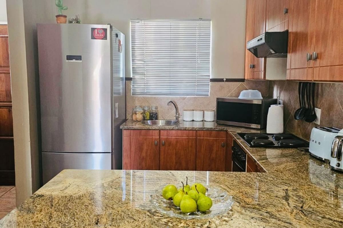 A functional kitchen featuring granite countertops, wooden cabinetry, and a built-in hob with an extractor fan.