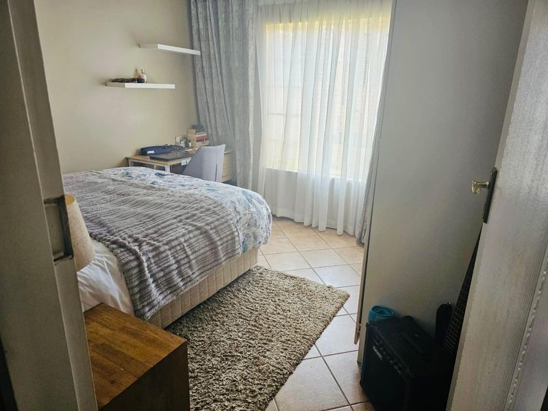 A functional bedroom featuring tiled flooring, built-in wall shelving, and large windows with curtain treatments, offering a comfortable and well-lit living space.