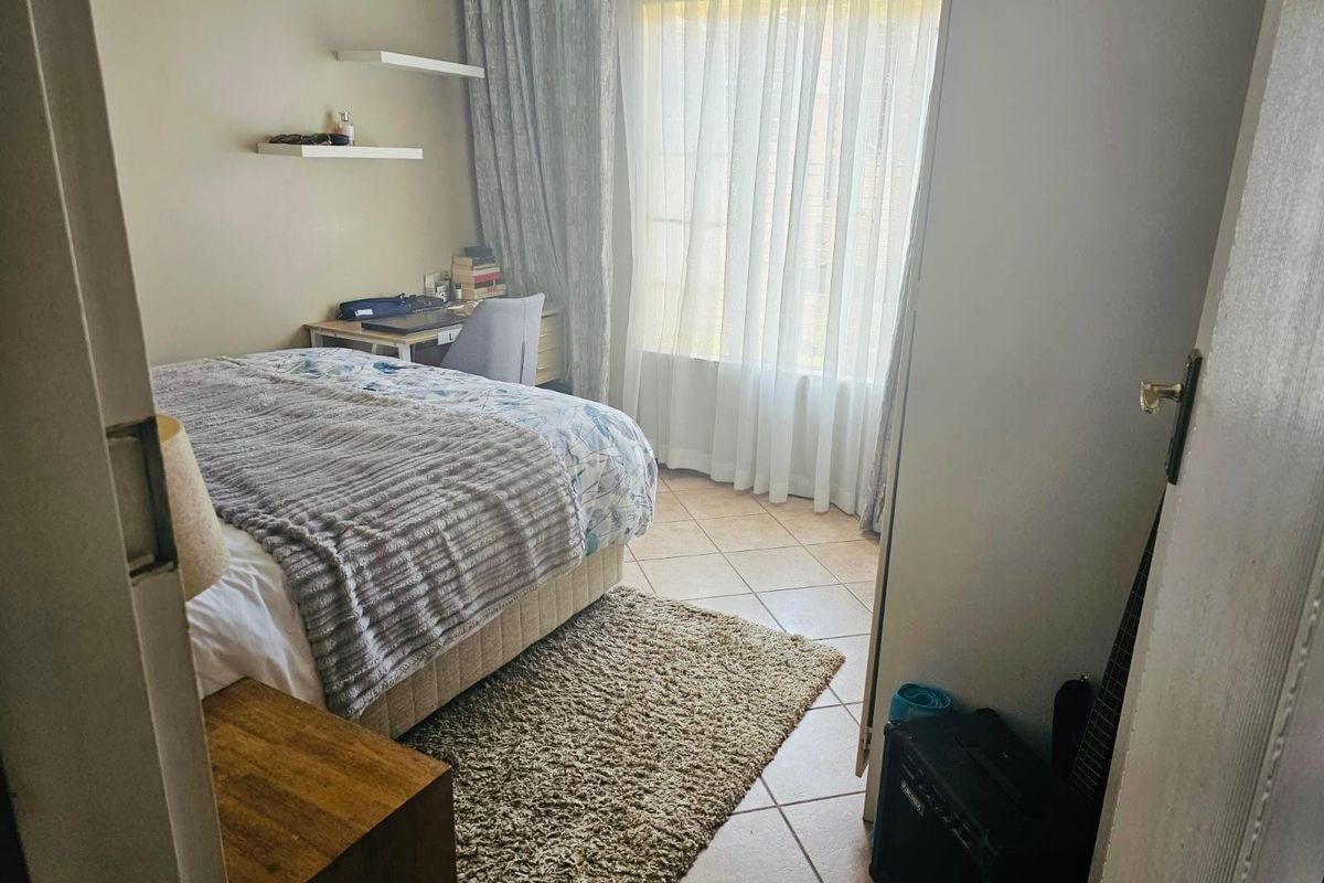 A functional bedroom featuring tiled flooring, built-in wall shelving, and large windows with curtain treatments, offering a comfortable and well-lit living space.