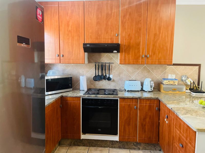 A functional kitchen featuring wooden cabinetry, granite countertops, a tiled backsplash, and built-in cooking appliances including an oven and electric hob.