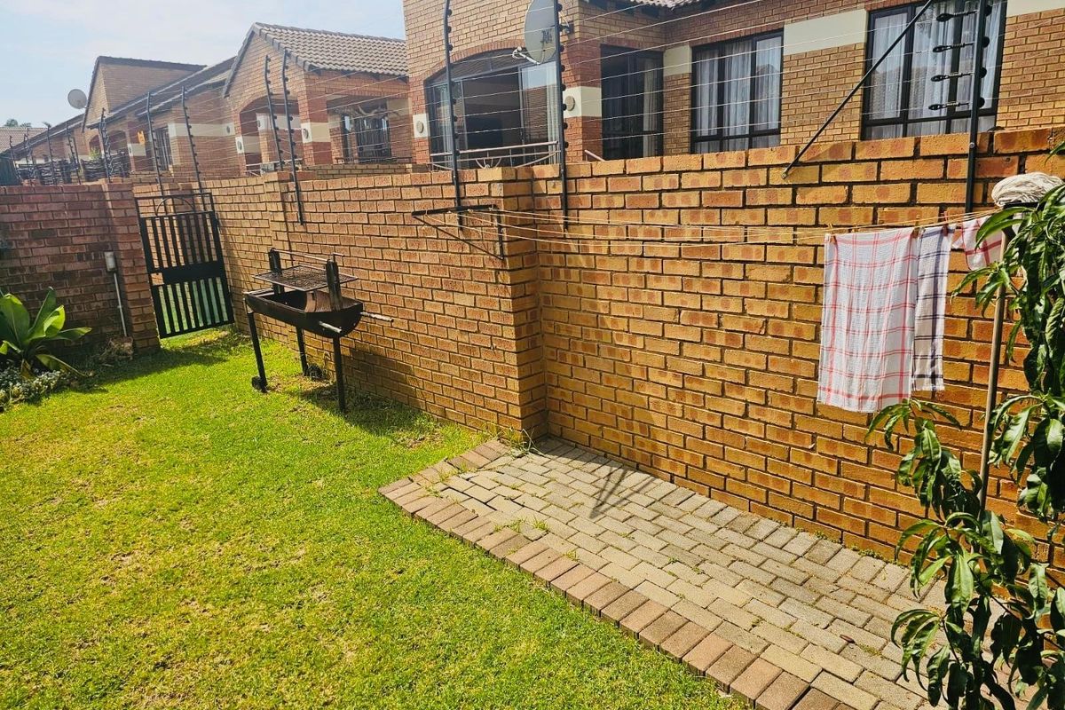 A private rear garden area featuring a face brick boundary wall with electric fencing, a paved walkway, and a small lawn.