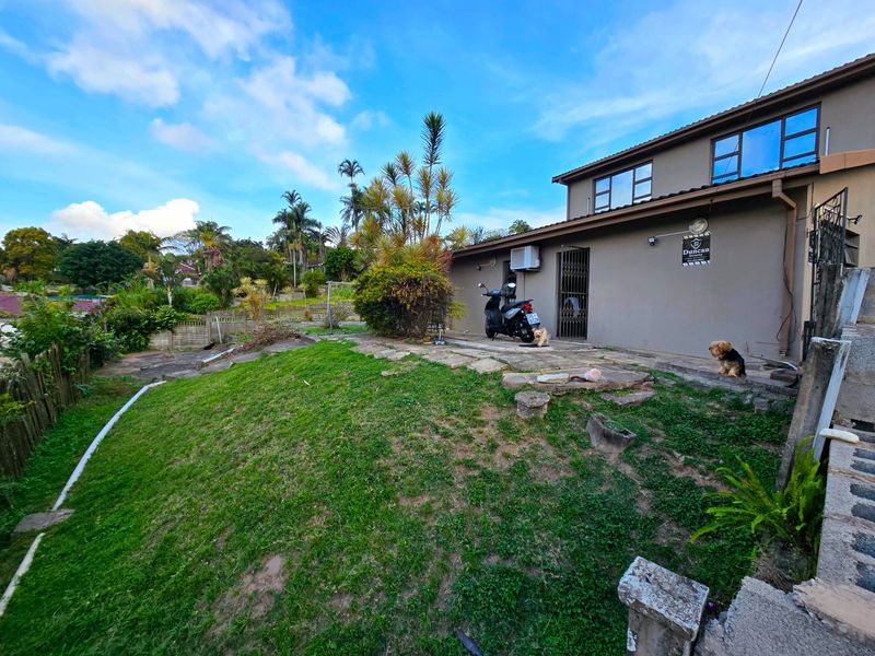 Rear exterior view of the property featuring a paved patio area, lawn, and security gate access.