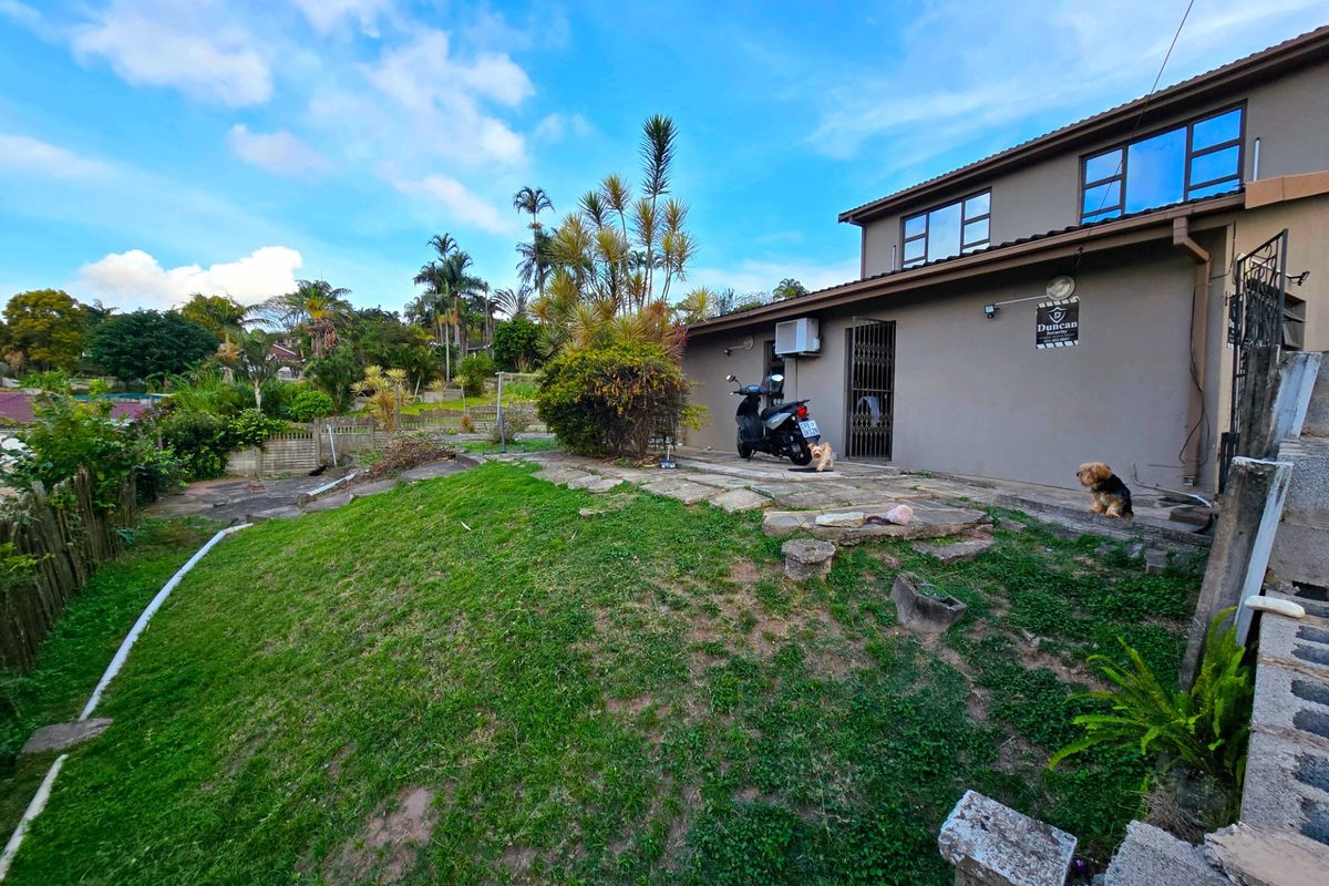 Rear exterior view of the property featuring a paved patio area, lawn, and security gate access.