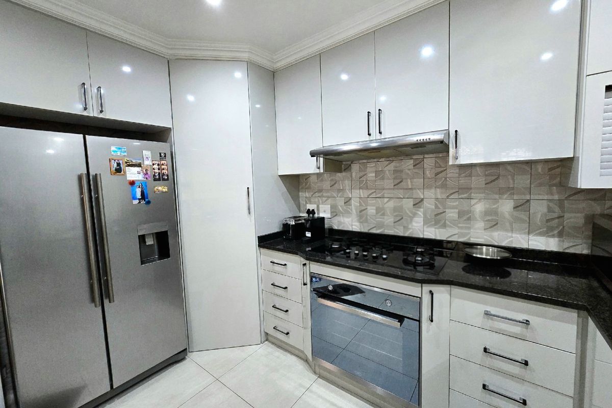 Modern kitchen featuring high-gloss cabinetry, granite countertops, a gas hob, built-in oven, and tiled flooring with a decorative backsplash.