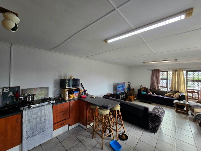 Open-plan living area featuring a kitchen with built-in cabinetry, a breakfast bar, and tiled flooring throughout, with security bars on the windows.