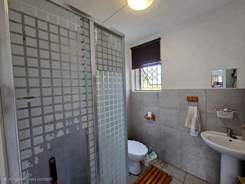 A functional bathroom featuring a shower enclosure, pedestal basin, toilet, and tiled wall finishes with a security gate on the window.