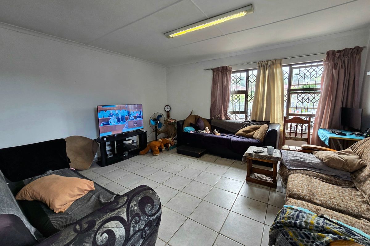 A living room featuring tiled flooring, security bars on the windows, and a fluorescent ceiling light fixture.