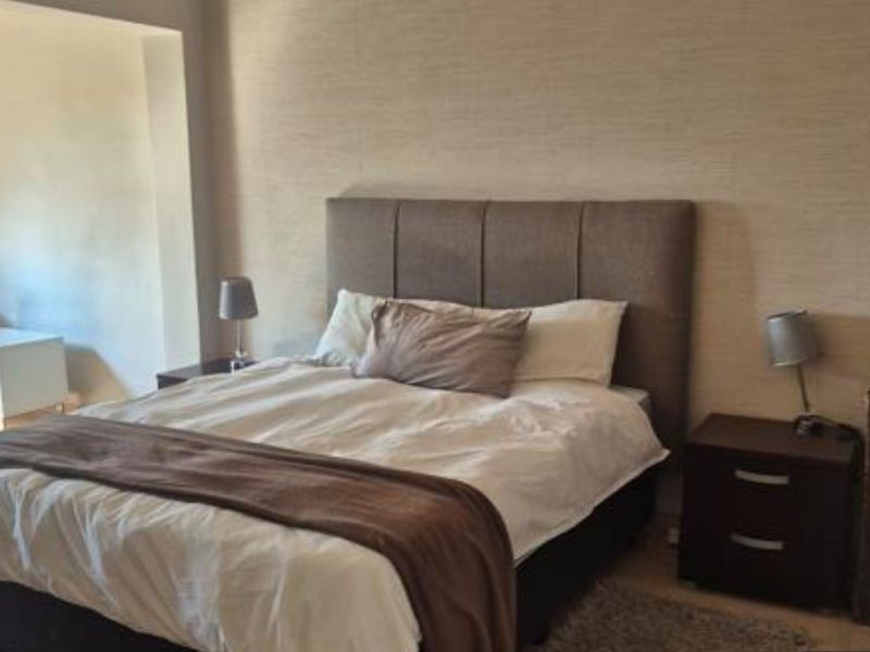 A comfortable bedroom featuring neutral textured wallpaper and a clean, modern aesthetic.