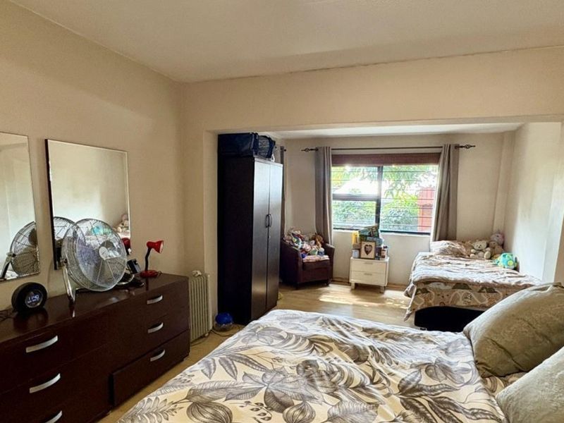 A spacious bedroom featuring laminate flooring, large wall-mounted mirrors, and an aluminium-framed window allowing natural light into the room.