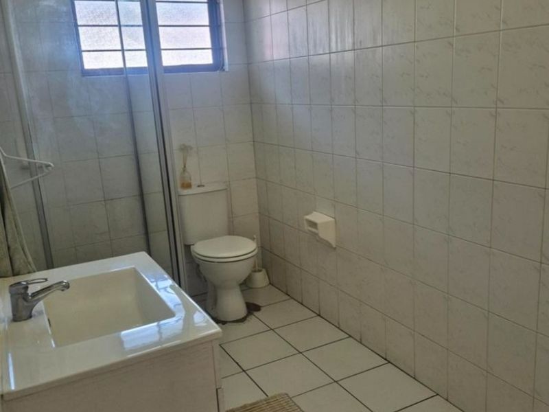 A functional bathroom featuring a shower enclosure, toilet, and vanity basin with white tiled walls and flooring.