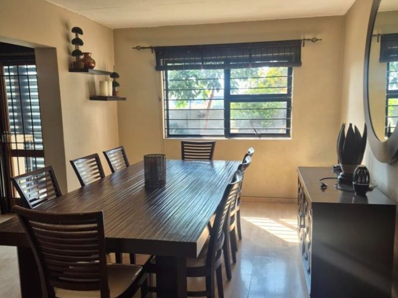A dining room featuring laminate flooring, security bars on the window, and track lighting, providing a functional space for meals.