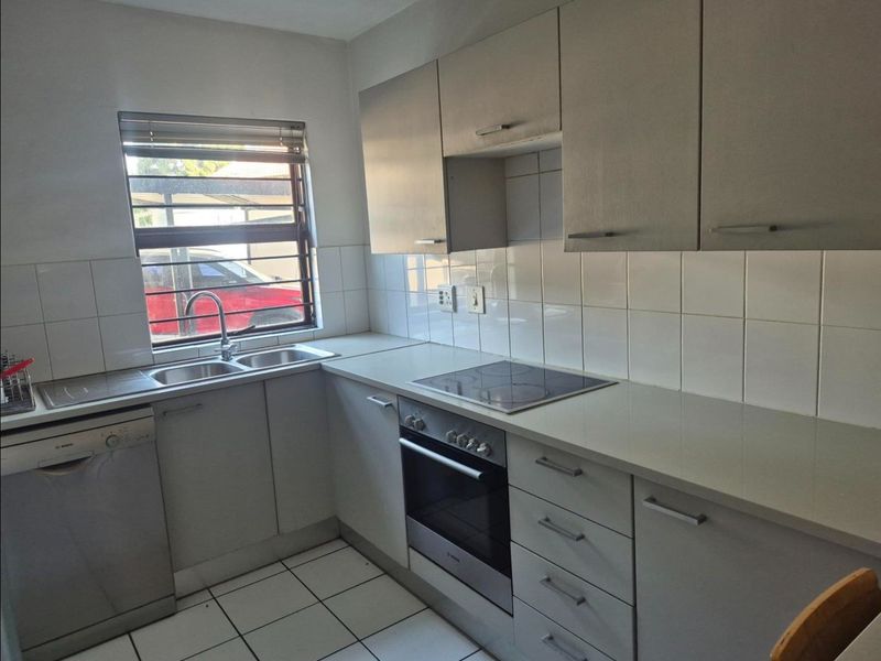 A functional kitchen featuring built-in cabinetry, a stainless steel sink, an electric hob, an oven, and tiled finishes throughout.