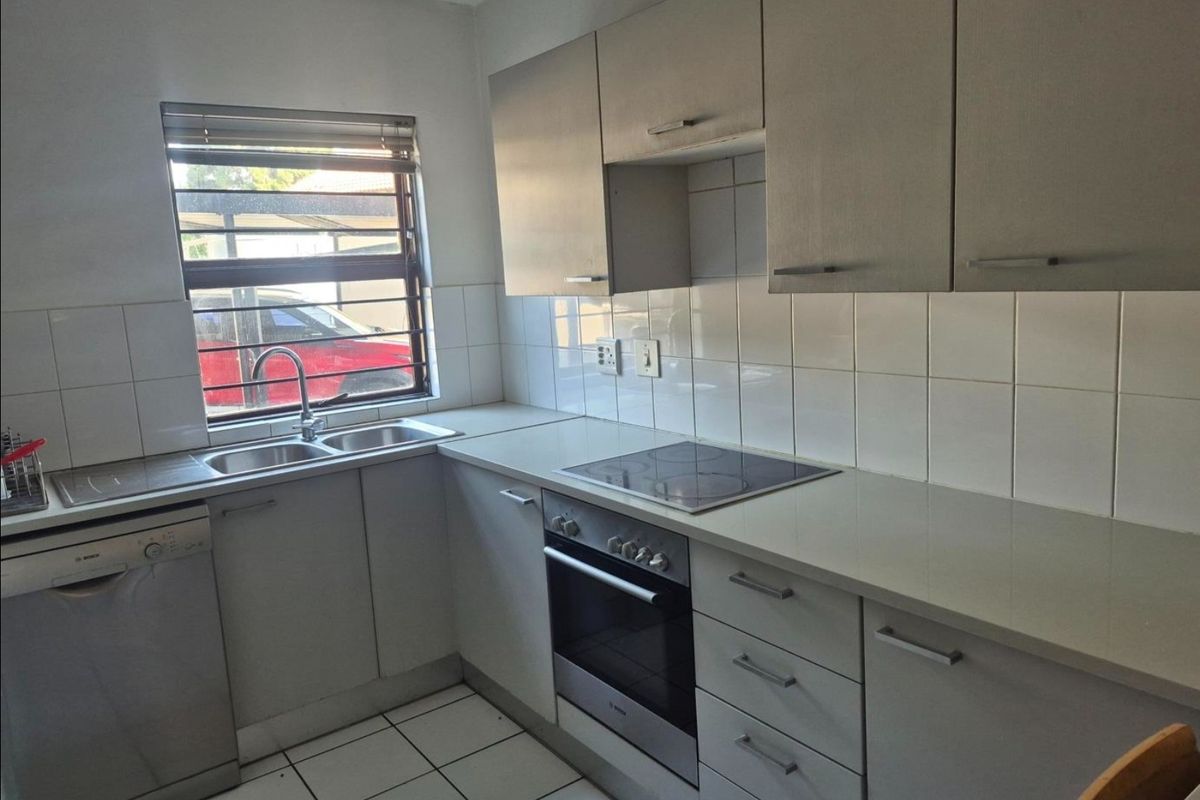 A functional kitchen featuring built-in cabinetry, a stainless steel sink, an electric hob, an oven, and tiled finishes throughout.