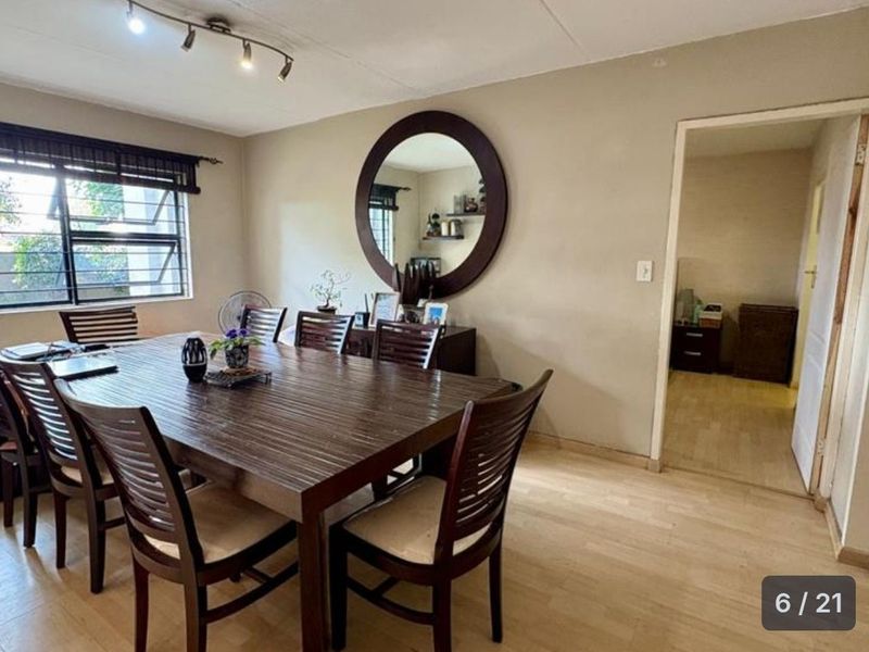A well-lit dining room featuring laminate flooring, track lighting, and an aluminium window frame, providing a functional space for family meals.