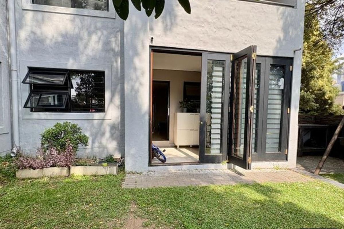 Rear view of the apartment featuring a paved patio area, lawn, and black-framed french doors leading into the interior living space.