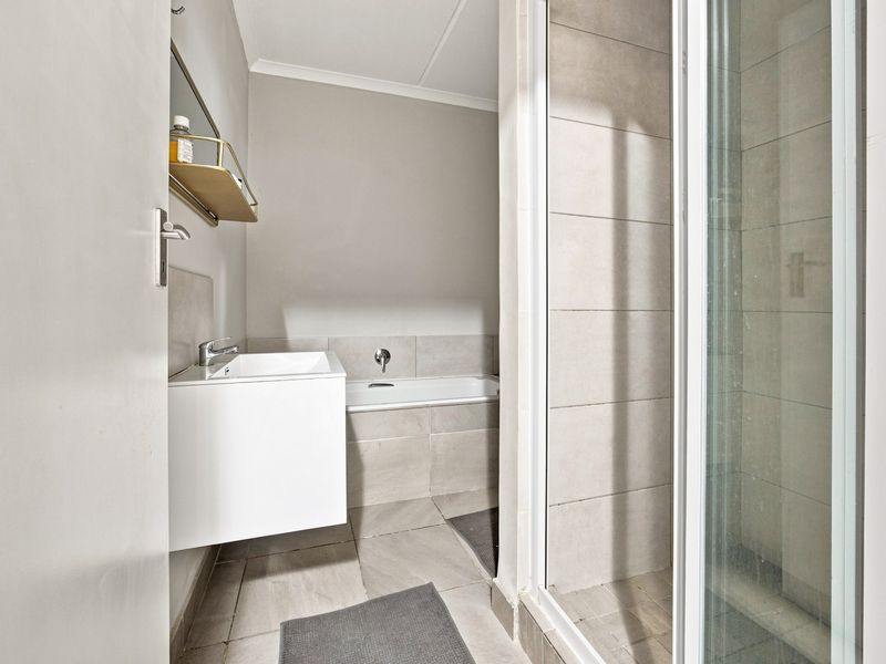 A clean, modern bathroom featuring a wall-mounted vanity, a built-in bathtub, and a separate shower enclosure with neutral tiling throughout.