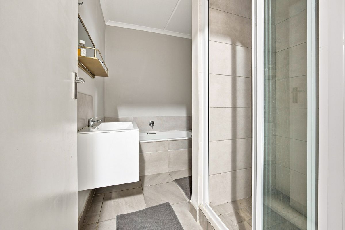 A clean, modern bathroom featuring a wall-mounted vanity, a built-in bathtub, and a separate shower enclosure with neutral tiling throughout.