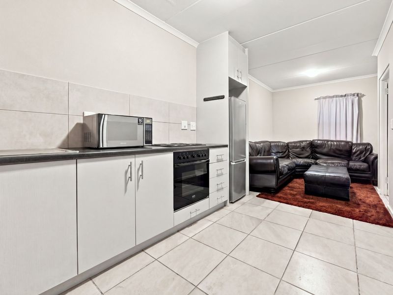 Open-plan living area featuring a functional kitchen with built-in cabinetry, oven, hob, and tiled flooring, seamlessly connected to the lounge space.
