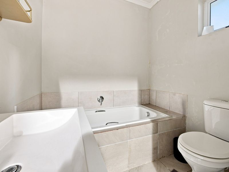A compact bathroom featuring a built-in bathtub, tiled surround, and standard toilet. The walls require cosmetic attention and repainting.