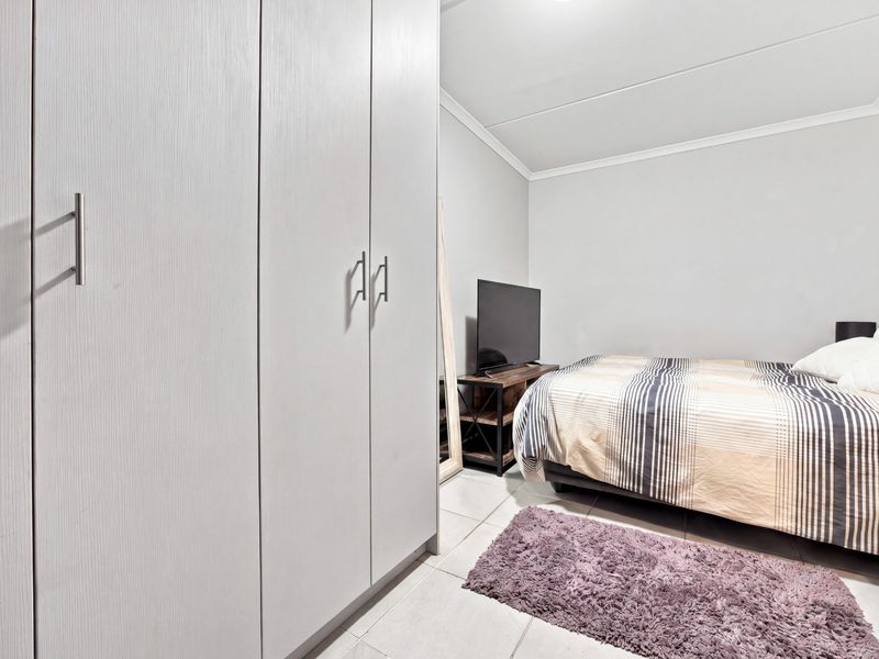 A well-maintained bedroom featuring neutral walls, tiled flooring, and a large built-in wardrobe with modern handles.