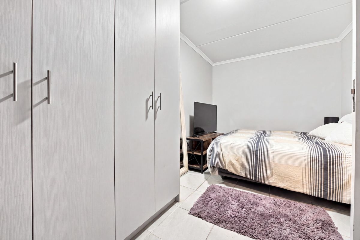 A well-maintained bedroom featuring neutral walls, tiled flooring, and a large built-in wardrobe with modern handles.