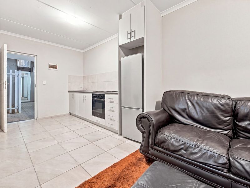 Open-plan living area featuring a compact kitchen with built-in cabinetry, oven, hob, and tiled flooring, leading to an exterior entrance.