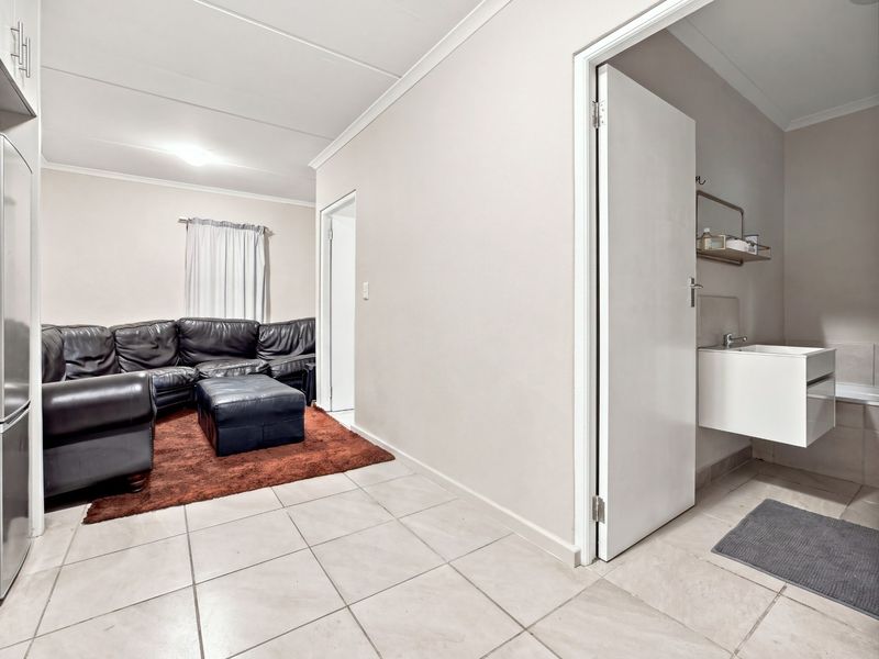 Open plan living area featuring tiled flooring, adjacent kitchen cabinetry, and a doorway leading to a bathroom with a modern wall-mounted vanity.