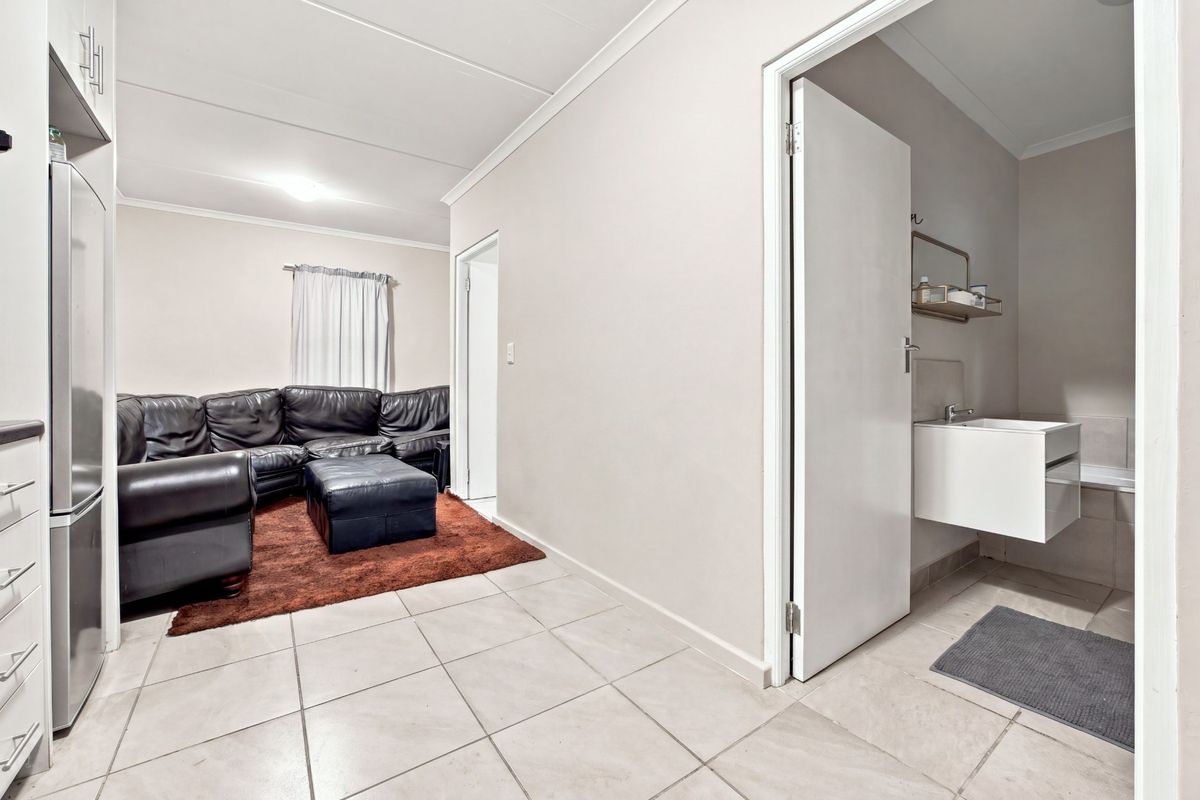 Open plan living area featuring tiled flooring, adjacent kitchen cabinetry, and a doorway leading to a bathroom with a modern wall-mounted vanity.