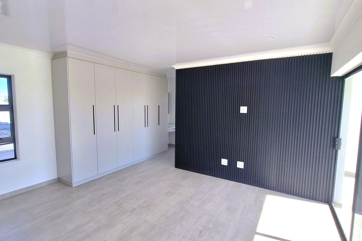 A modern, empty bedroom featuring built-in cupboards, a stylish black slatted feature wall, tiled flooring, and access to an outdoor area via sliding doors.