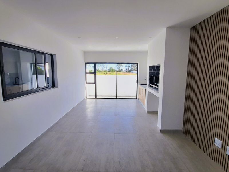 Modern open-plan living area featuring tiled floors, a built-in braai, decorative slat wall paneling, and large sliding doors leading to the exterior.