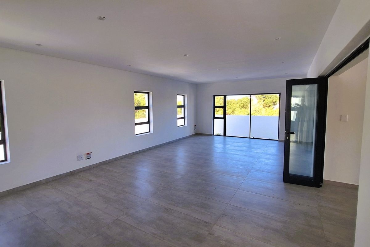 A spacious, empty living area featuring modern grey floor tiles, recessed lighting, and large aluminium-framed windows and sliding doors providing ample natural light.