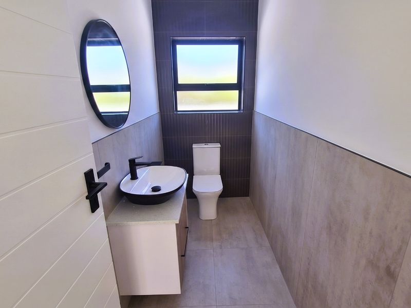 Modern guest bathroom featuring a sleek vanity with vessel sink, black fixtures, and contemporary neutral wall and floor tiling.