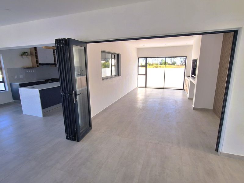 Spacious open-plan living and kitchen area featuring modern tiled flooring, sleek cabinetry, and large bi-fold doors opening to the exterior.