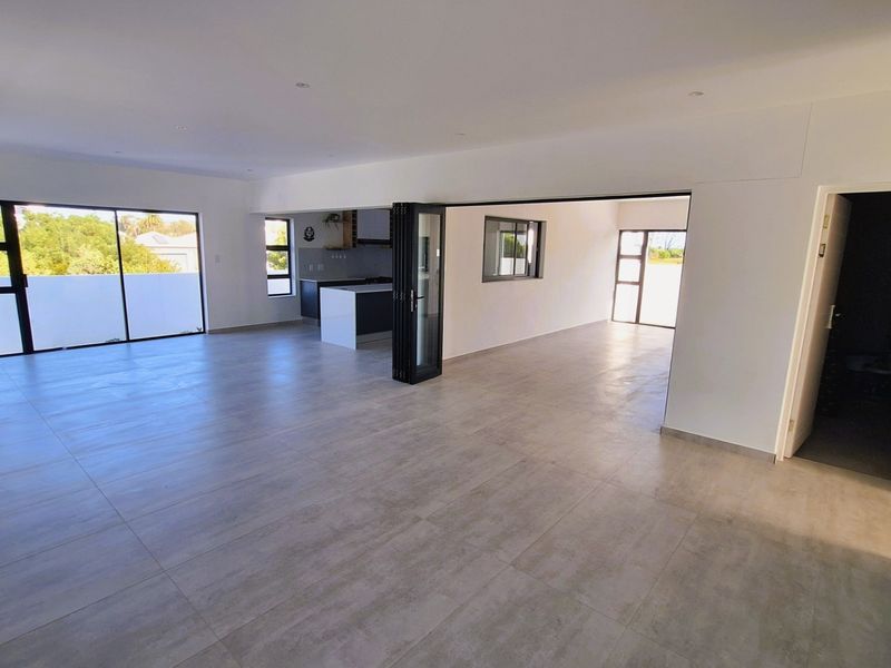 Spacious open-plan living area featuring modern tiled floors, recessed lighting, and seamless flow to the kitchen, with large aluminium doors providing ample natural light.