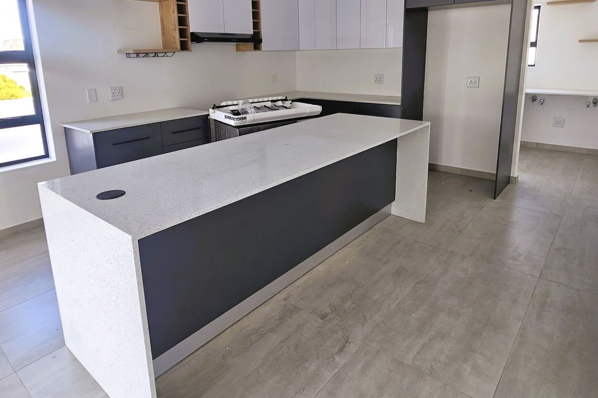 Modern kitchen featuring a large quartz island, sleek cabinetry, gas hob, and tiled flooring, offering a clean and contemporary space.