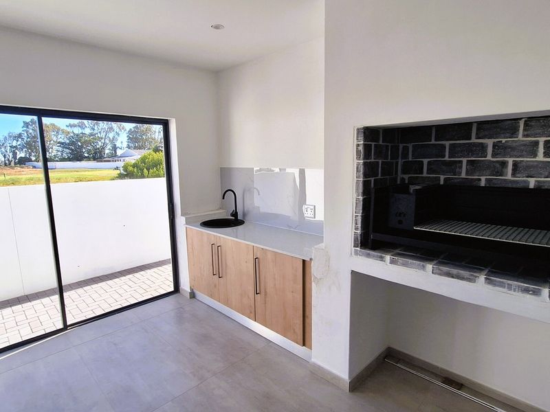 Covered patio area featuring a built-in braai, modern cabinetry with stone countertop, sink, and large sliding doors leading to an outdoor space.