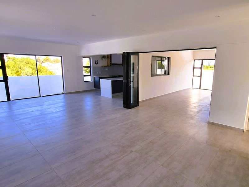 Spacious open-plan living area featuring modern tiled floors, recessed lighting, and seamless flow to the kitchen, enhanced by large aluminium sliding and bi-fold doors.
