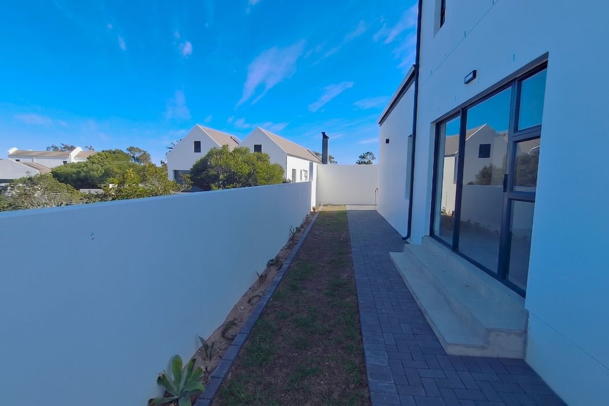 A rear exterior view featuring a paved walkway, boundary wall, and large sliding glass doors leading into the home.