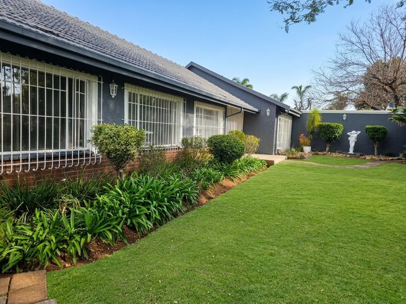 A well-maintained rear exterior view of the house featuring a manicured lawn, landscaped garden beds, and secure window bars.