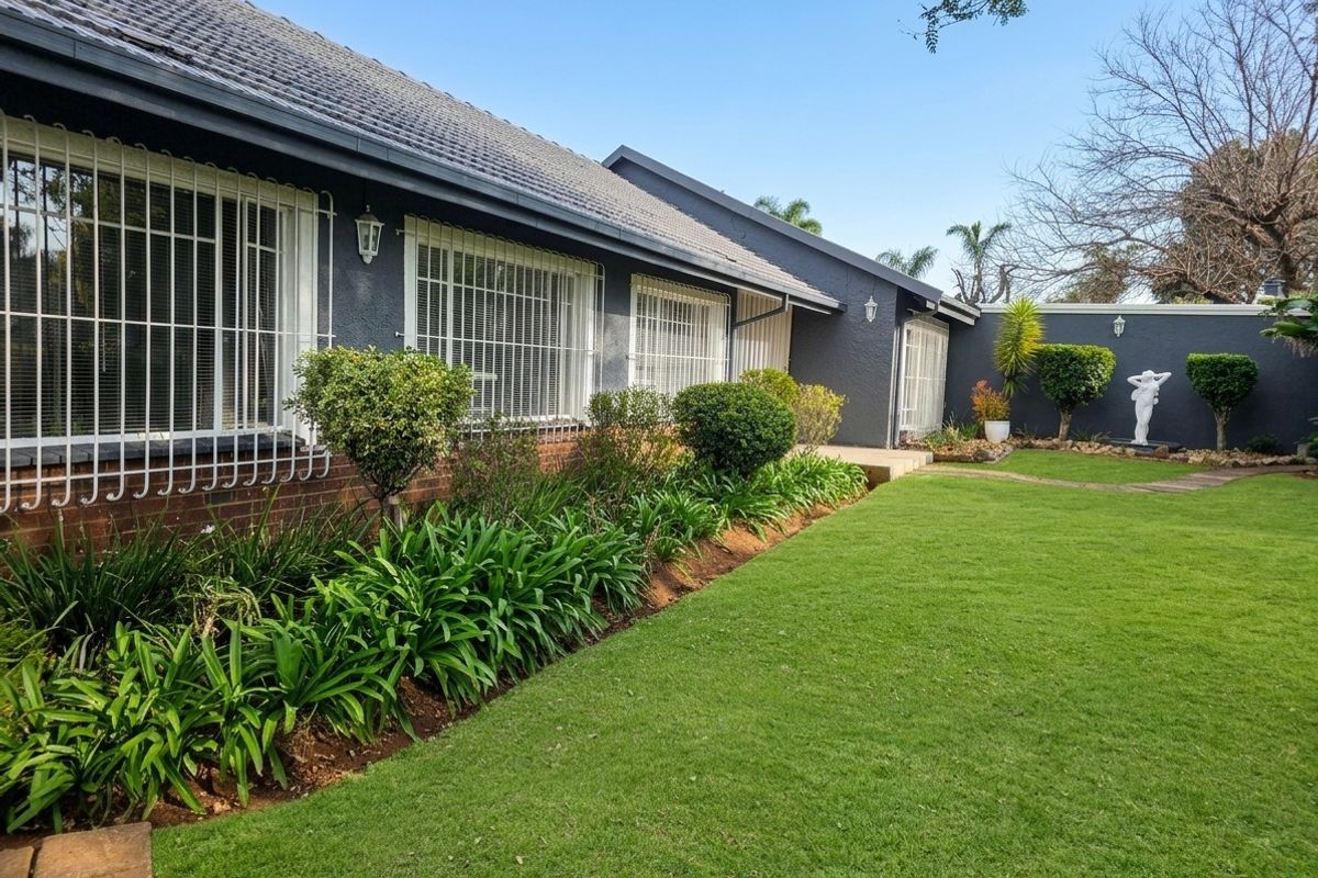 A well-maintained rear exterior view of the house featuring a manicured lawn, landscaped garden beds, and secure window bars.