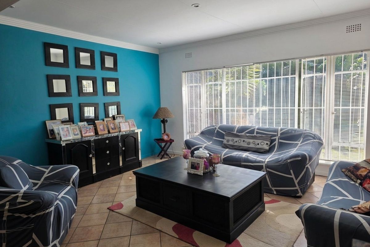 A bright living room featuring tiled flooring, crown molding, and large windows fitted with security bars, offering a functional and well-lit space.