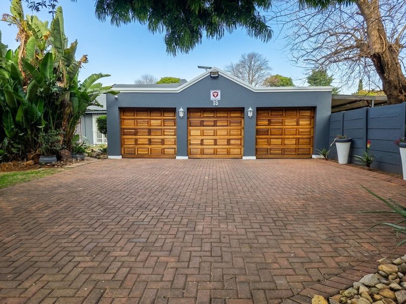 A well-maintained front exterior featuring a triple garage with timber doors and a spacious paved driveway.