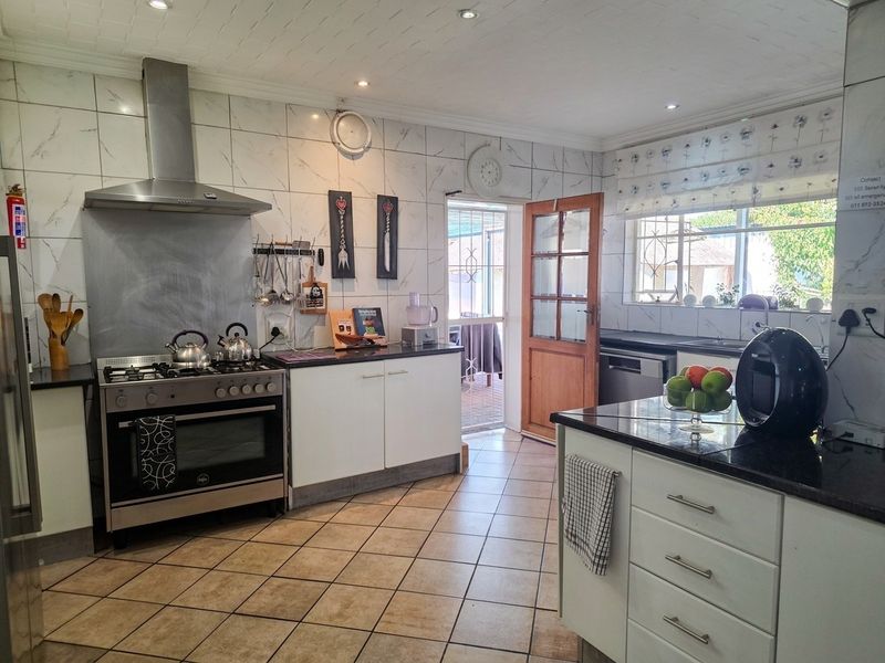 A functional kitchen featuring granite countertops, tiled walls, a gas stove with extractor fan, and direct access to an outdoor area.