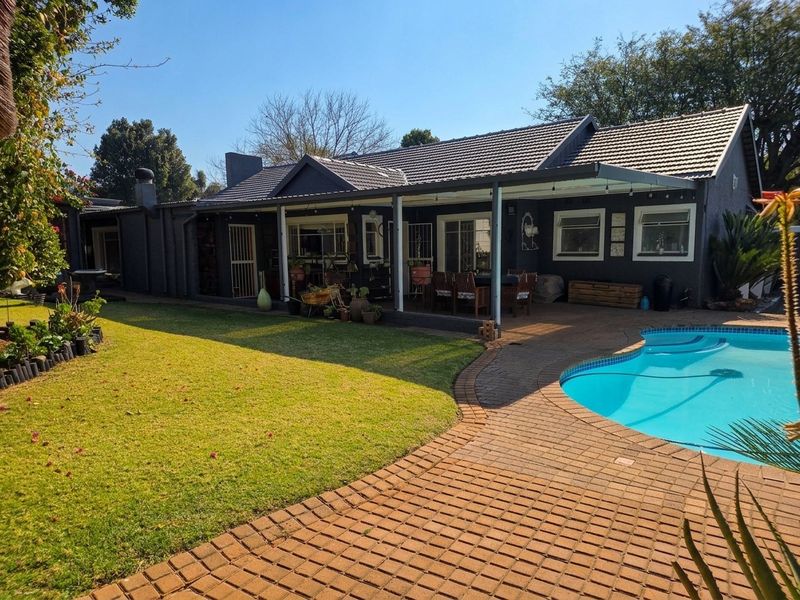 Rear view of the property featuring a covered patio, paved pool area, swimming pool, and a well-maintained garden.