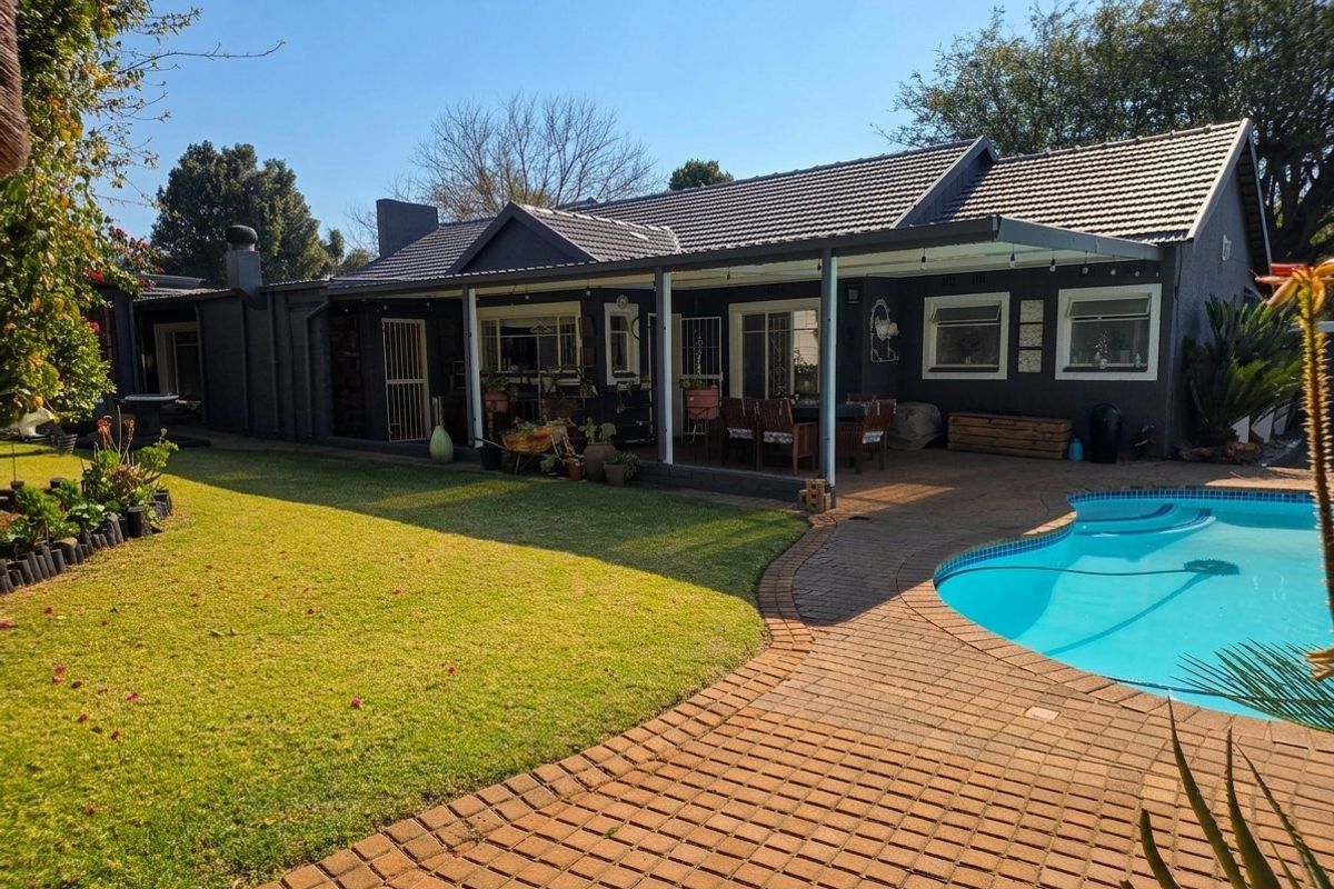 Rear view of the property featuring a covered patio, paved pool area, swimming pool, and a well-maintained garden.