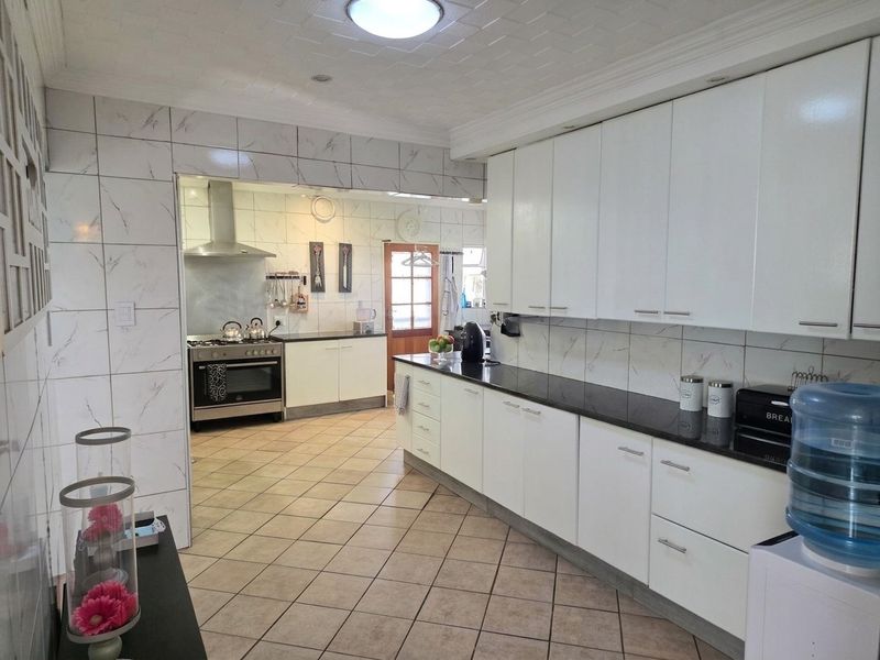 Spacious kitchen featuring white cabinetry, dark stone countertops, tiled splashbacks, and a gas stove with extractor fan, leading into a secondary prep area.
