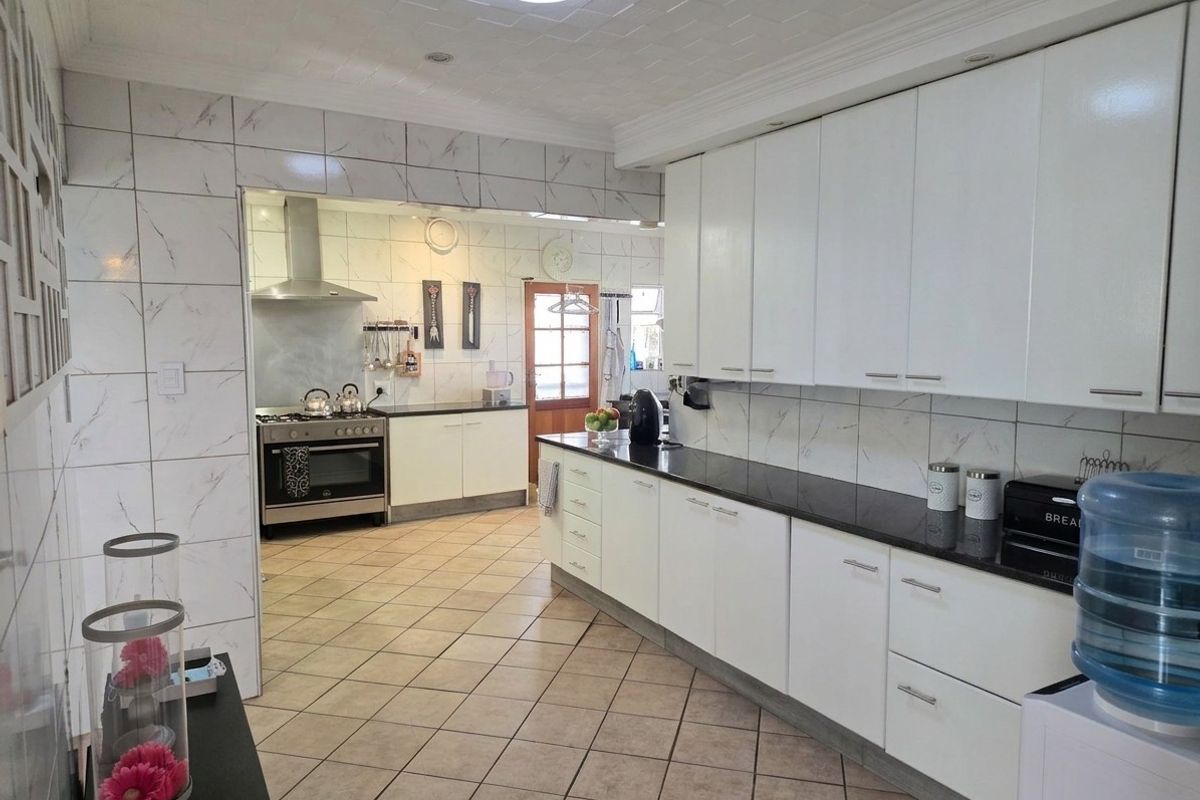 Spacious kitchen featuring white cabinetry, dark stone countertops, tiled splashbacks, and a gas stove with extractor fan, leading into a secondary prep area.